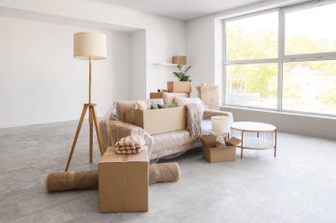 Karton kutularla kaplı kanepe ve taşınma günü odasındaki eşyalar.