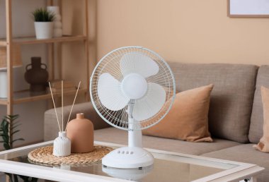 Oturma odasındaki kanepenin yanındaki masada elektrikli vantilatör var.