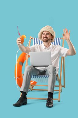 Dizüstü bilgisayarı ve mavi arka planda el sallayan genç iş adamı. Yaz tatili kavramı