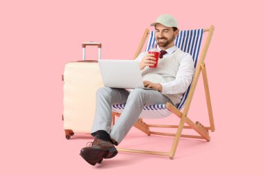 Kokteyl kullanan iş adamı pembe arka planda dizüstü bilgisayar kullanıyor. Yaz tatili kavramı