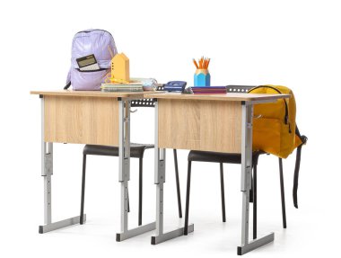 Beyaz zemin üzerinde kırtasiye ve sırt çantaları olan okul sıraları