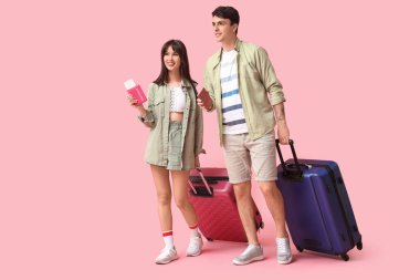 Pasaportları ve bavulları olan birkaç turist pembe arka planda yürüyor.