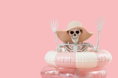 Pembe arka planda yüzme yüzükleri ve şapkası olan insan iskeleti. Yaz tatili kavramı