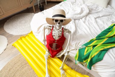 Yatak odasında plaj aksesuarları olan insan iskeleti. Yaz tatili kavramı