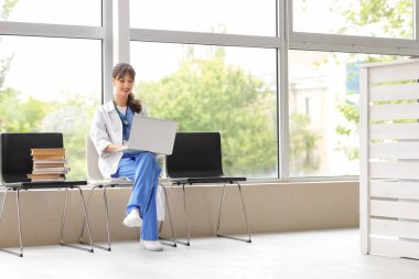 Klinikteki sandalyede dizüstü bilgisayar kullanan kadın stajyer.