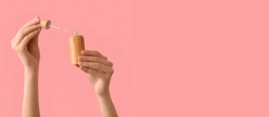 Female hands with bottle of cosmetic product on pink background