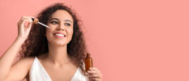 Güzel genç Afro-Amerikalı kadın pembe arka planda kozmetik yağ kullanıyor ve metin için yer var.