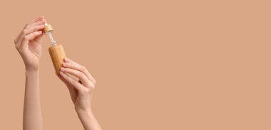 Kahverengi arka planda kozmetik ürünü şişesi olan kadın elleri