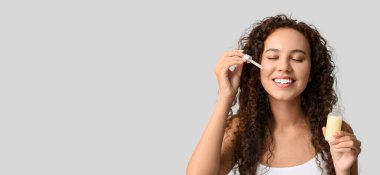 Güzel genç Afro-Amerikalı kadın yüzüne kozmetik yağ sürerken arka plan aydınlık ve metin için yer var.