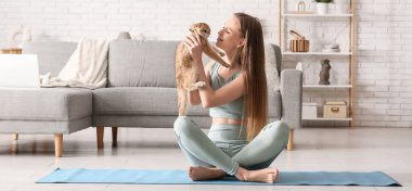 Evde yoga minderinde oturan sevimli kedisi olan genç bir kadın.