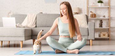 Evde yoga minderinde oturan sevimli kedisi olan genç bir kadın.