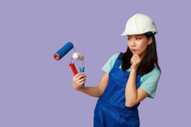 Mor arka planda silindirleri olan Asyalı düşünceli bir kadın ressam.