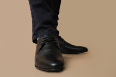 Kahverengi arka planda siyah şık ayakkabılı genç adamın bacakları.