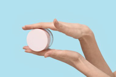 Mavi arka planda yüz kremi kavanozu olan kadın elleri