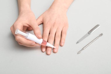 Gri arka planda kalem ve manikür aletleriyle tırnak altı yağı uygulayan kadın eller