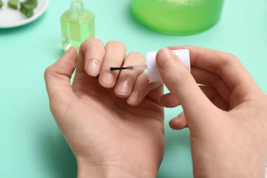 Turkuaz arka planda tırnaklarına tırnak yağı süren kadın, yakın plan.