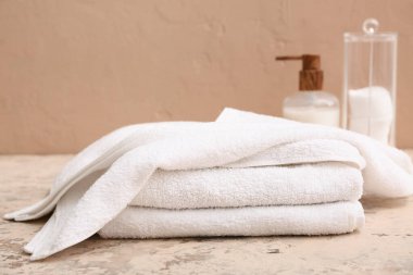 Temiz yumuşak havlular, bir şişe kozmetik ürünü ve kahverengi duvarın yanında pamuk yastıklı tutucu.