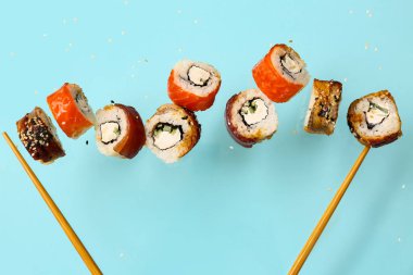 Mavi arka planda lezzetli uçan suşi ruloları ve çubuklar.
