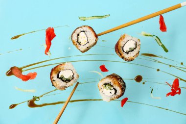 Lezzetli uçan suşi ruloları, soya sosu ve mavi arka planda çubuklar.