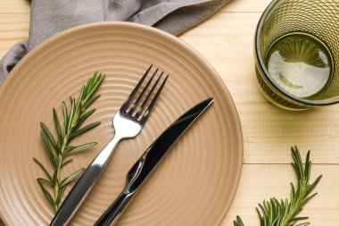 Ahşap zemin üzerinde peçete, çatal bıçak, cam ve biberiye ile şık masa ayarları