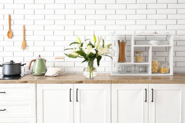 Mutfaktaki ahşap tezgahta güzel zambak çiçekleri olan vazo.