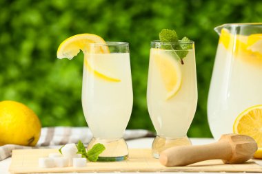 Bardaklar ve bir sürahi taze limonata ve açık havada beyaz ahşap masa üzerinde nane şekeri.