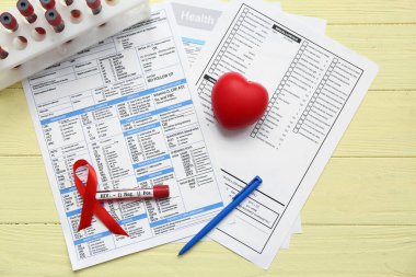 HIV testi tüpleri, laboratuvar raporu formu, sarı ahşap arka planda kalp ve kırmızı kurdele.