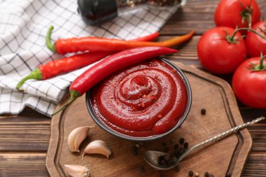 Bir kase kırmızı biber sosu ve ahşap arka planda farklı malzemeler.