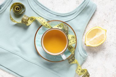 Bir fincan diyet çay, mezura, limon ve arka planda şık spor bluzu. Kilo verme konsepti