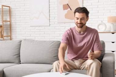 Şeker hastası, elinde tükenmez kalemle masadan glukometre alıyor.