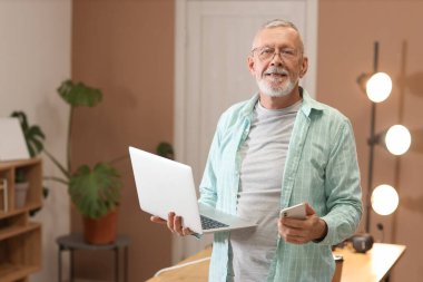 Akşam ofiste dizüstü bilgisayar ve cep telefonuyla çalışan yetişkin programcı