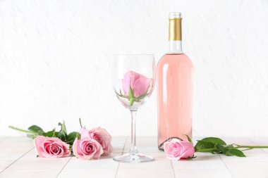 Bir şişe pembe şarap, cam ve beyaz fayans üzerinde güzel güller.