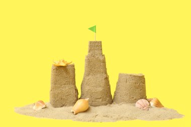 Güzel kumdan kale, sarı arka planda deniz kabukları.