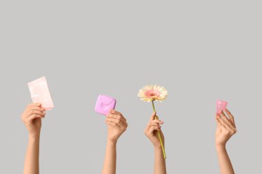 Gri arka planda regl bardağı, ped ve tampon saklama kutusu olan kadın elleri
