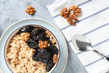 Bir kase lezzetli yulaf ezmesi, arkaplanda kuru erik, ceviz ve kaşık.