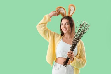 Beautiful young woman in bunny ears with pussy willow branches on green background