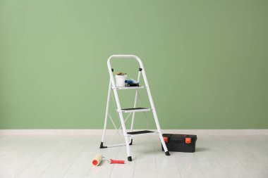 Odada yeşil duvarın yanında boya aletleri olan merdiven.