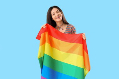Mavi arka planda gökkuşağı bayrağı olan güzel genç bir kadın. LGBT kavramı