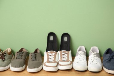 Yeşil duvarın yanındaki bankta ortopedik tabanlı spor ayakkabılar.