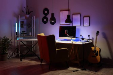 Karanlık kayıt stüdyosunun içinde işyeri, müzik aletleri ve parlayan lambalar var.