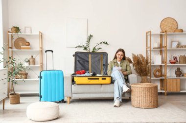 Kadın turist evdeki kanepede bavul hazırlarken kontrol listesi yapıyor.