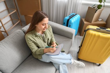 Bavullu genç bir kadın taşınma gününde odada kontrol listesi yapıyor.