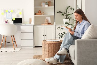 Genç bir kadın evdeki kanepede yapılacaklar listesi yapıyor.