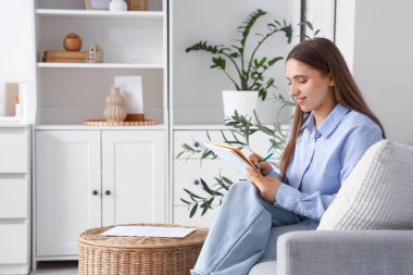 Genç bir kadın evdeki kanepede yapılacaklar listesi yapıyor.