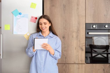 Mutfakta buzdolabının yanında yapılacaklar listesi hazırlayan genç bir kadın.