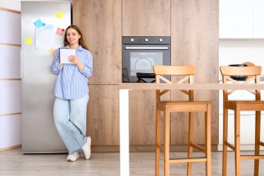 Mutfakta buzdolabının yanında yapılacaklar listesi hazırlayan genç bir kadın.