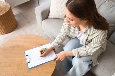 Genç bir kadın evdeki kanepede yapılacaklar listesi yapıyor.