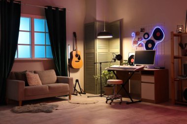 Karanlık kayıt stüdyosunun içinde işyeri, müzik aletleri ve parlayan lambalar var.