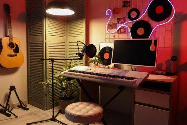 Karanlık kayıt stüdyosunun içinde işyeri, müzik aletleri ve parlayan lambalar var.