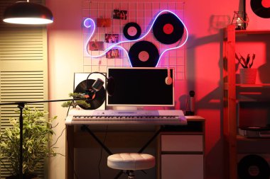 Karanlık kayıt stüdyosunun içinde işyeri, sentezleyici ve parlayan lambalar var.